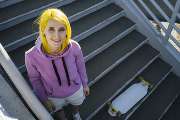 Dyed hair hipster female with skateboard standing on staircase during sunny day - VPIF03164