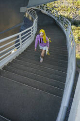 Young woman holding skateboard climbing steps on sunny day - VPIF03165