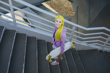 Young woman standing with skateboard on staircase during sunny day - VPIF03166