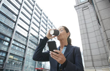 Geschäftsfrau trinkt Kaffee und benutzt ein Mobiltelefon in der Stadt - PMF01326