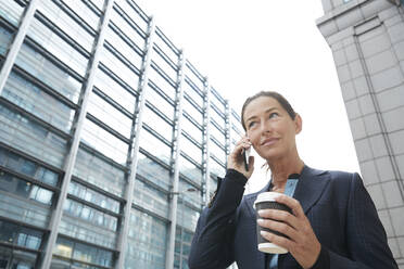 Smiling businesswoman drinking coffee while talking on mobile phone in city - PMF01328