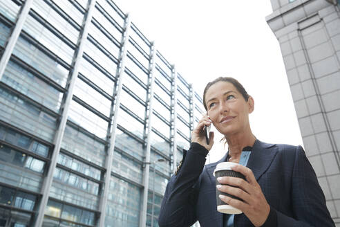 Lächelnde Geschäftsfrau, die Kaffee trinkt und mit dem Handy in der Stadt telefoniert - PMF01328