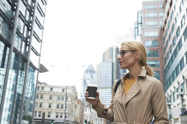 Businesswoman with coffee cup looking away while standing in city - PMF01330