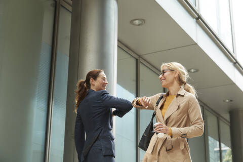 Businesswoman and colleague greeting with elbow bump while standing in city stock photo