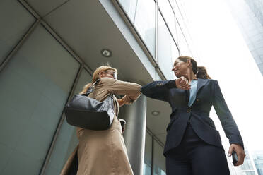 Colleague and businesswoman greeting with elbow bump while standing in city - PMF01334