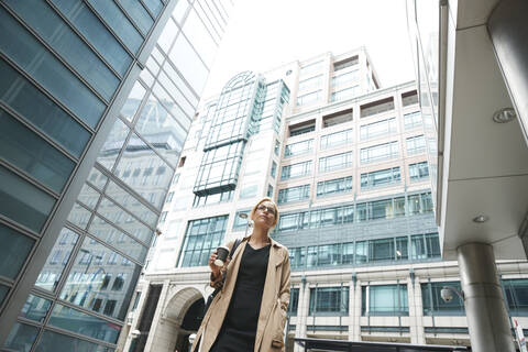 Businesswoman with coffee cup and hand in pocket standing in city stock photo