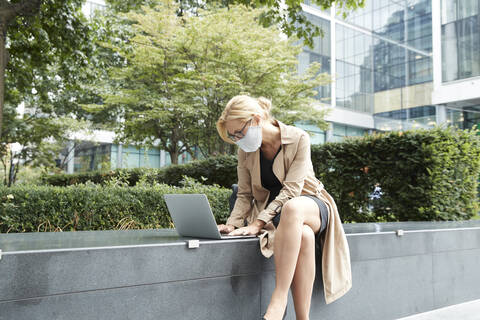 Businesswoman wearing face mask working on laptop in city stock photo