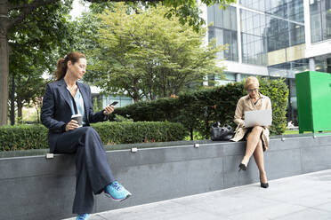 Geschäftsfrauen halten soziale Distanz, während sie im Büropark sitzen - PMF01352