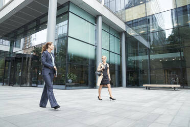 Colleague talking while walking against office building exterior - PMF01362