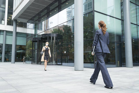 Business people wearing face mask while walking against office building stock photo