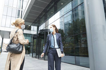 Women wearing face mask talking while standing against office building - PMF01372