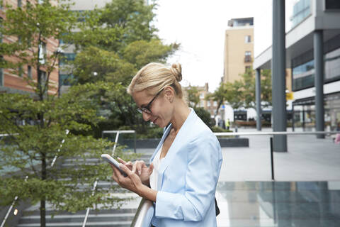 Woman using mobile phone while standing at railing in city stock photo