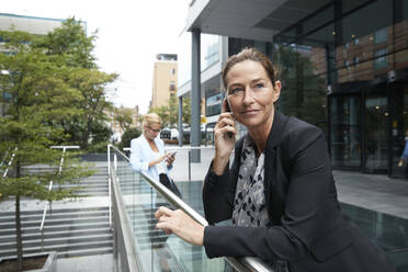 Frau, die mit einem Mobiltelefon spricht, während ein Kollege im Hintergrund in der Stadt steht - PMF01401