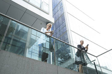 Women using mobile phone while leaning on railing against building - PMF01403