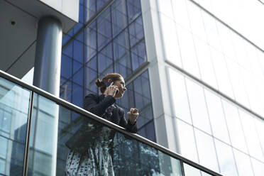 Businesswoman talking on mobile phone while leaning on railing against building - PMF01406