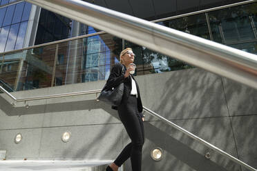 Mature woman with coffee cup walking on staircase against building exterior - PMF01411