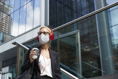Businesswoman with coffee cup listening music while standing against building stock photo