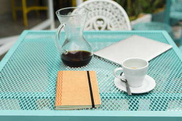 Table with notepad, laptop, coffee cup and pot at cafe - JMPF00451