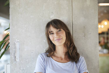 Smiling woman standing against concrete wall at home - FMKF06492