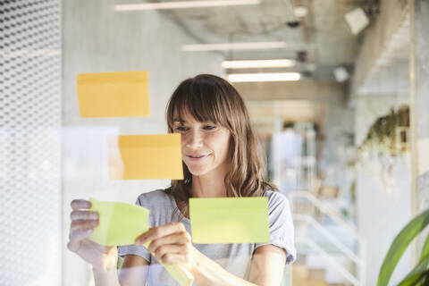 Smiling mature woman sticking adhesive notes on glass material stock photo