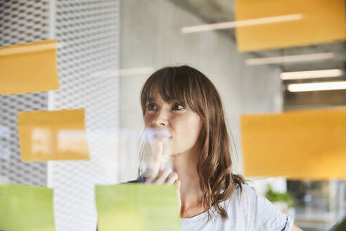 Thoughtful woman with hand on chin looking at sticky notes - FMKF06514