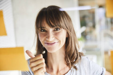 Mature woman gesturing while looking at sticky notes stick on glass material stock photo