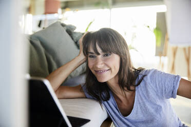 Woman with hands in hair using digital tablet at home - FMKF06520