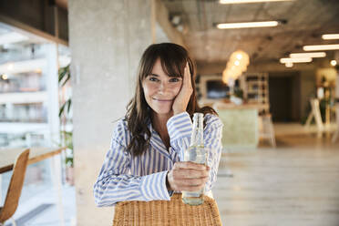 Mature woman with head in hands holding beer bottle while sitting at home - FMKF06542