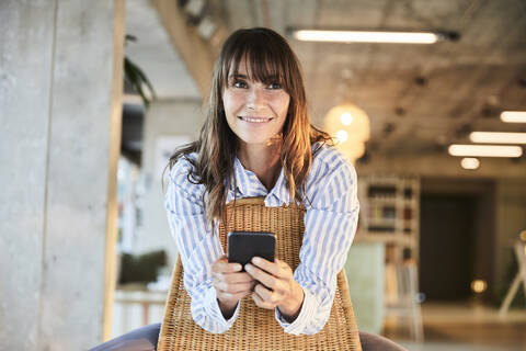 Mature woman smiling while using smart phone sitting at home stock photo