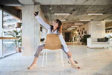 Reife Frau, die ein Selfie mit ihrem Smartphone macht, während sie zu Hause sitzt - FMKF06548