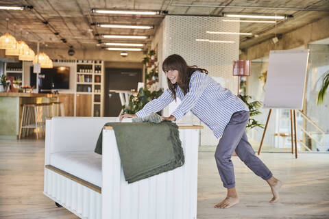 Smiling mature woman pushing sofa at home stock photo