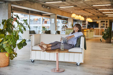 Smiling woman using digital tablet while sitting on sofa at modern home - FMKF06560