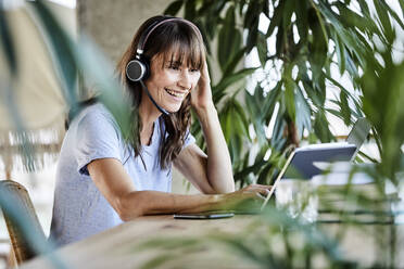 Smiling woman with headphones using digital tablet while sitting by table at home - FMKF06566