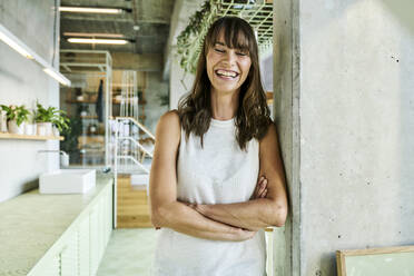 Smiling woman with eyes closed and arms crossed standing at home - FMKF06576