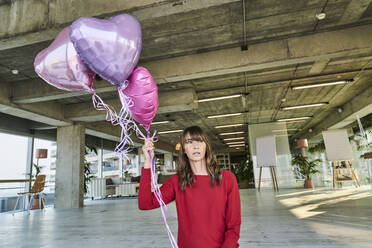 Businesswoman holding balloons while standing in loft office - FMKF06602