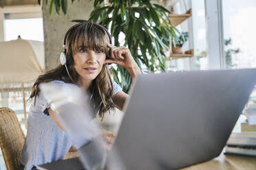 Woman with head in hands working on laptop at home - FMKF06609