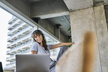 Woman with headphones looking at laptop while sitting at home - FMKF06615