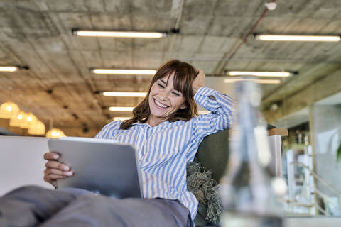 Smiling woman with hand in hands using digital tablet while sitting on sofa at home stock photo