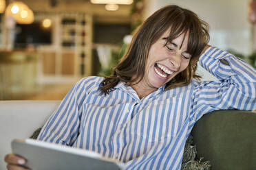 Frau lachend bei der Verwendung eines digitalen Tablets zu Hause - FMKF06628
