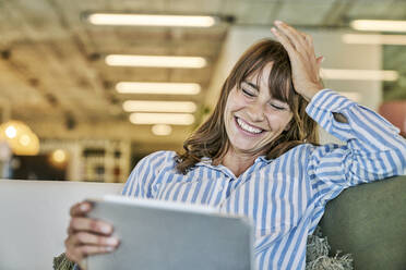 Frau mit Kopf in der Hand lachend bei der Verwendung eines digitalen Tablets zu Hause - FMKF06630