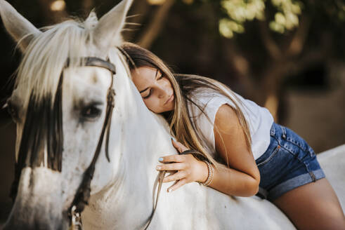 Portrait of beautiful young woman riding horse with large teddy