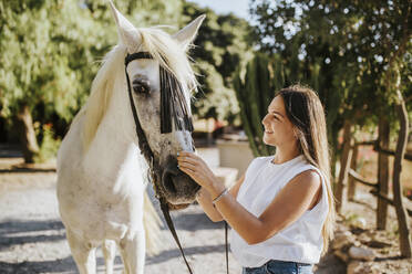 Beautiful young woman gently stroking white horse - MIMFF00240