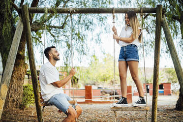 Young couple spending time on swings in public park - MIMFF00246