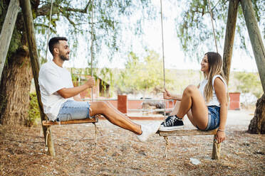 Junges Paar verbringt Zeit auf einer Schaukel in einem öffentlichen Park - MIMFF00247