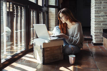Redhead woman working on laptop while sitting on floor at home - JSMF01809