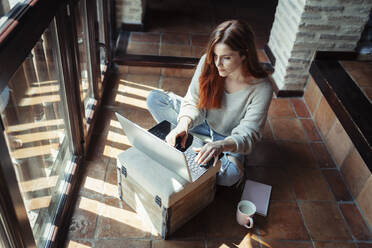 Woman working on laptop while sitting on floor at home - JSMF01811