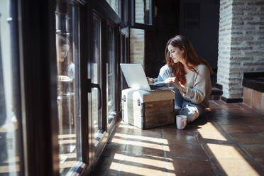 Young woman working on laptop while sitting on floor at home - JSMF01812