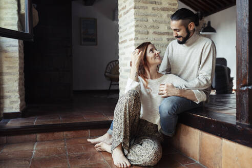 Man looking at smiling woman sitting on floor at home - JSMF01831