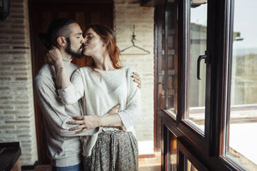 Couple kissing while standing by window at home - JSMF01838