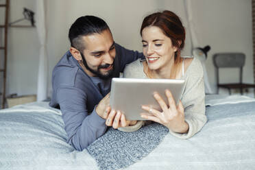 Smiling couple using digital tablet while lying on bed at home - JSMF01840